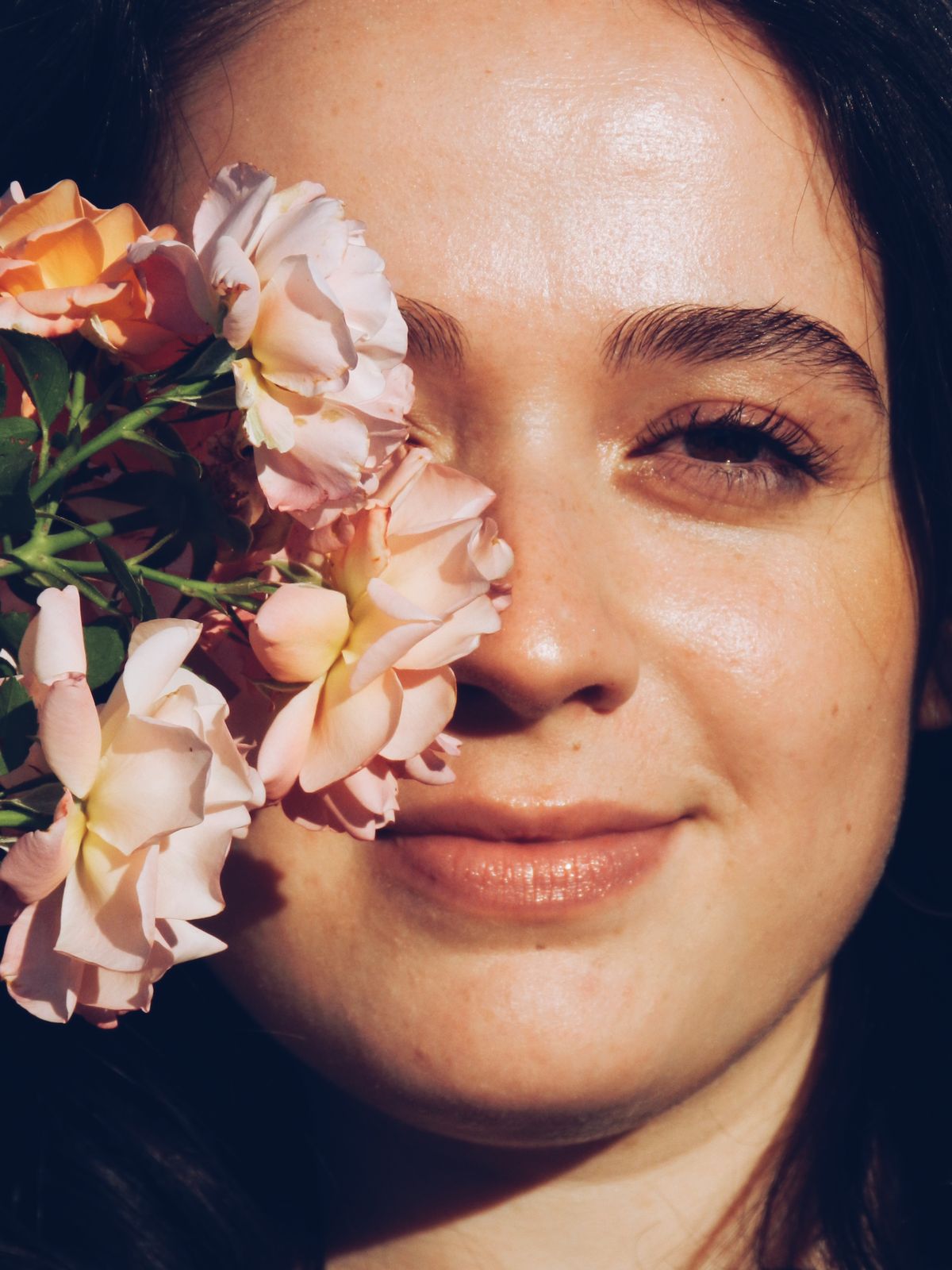 Femme au teint lumineux avec des fleurs près du visage, illustrant la beauté et l'éclat de la peau