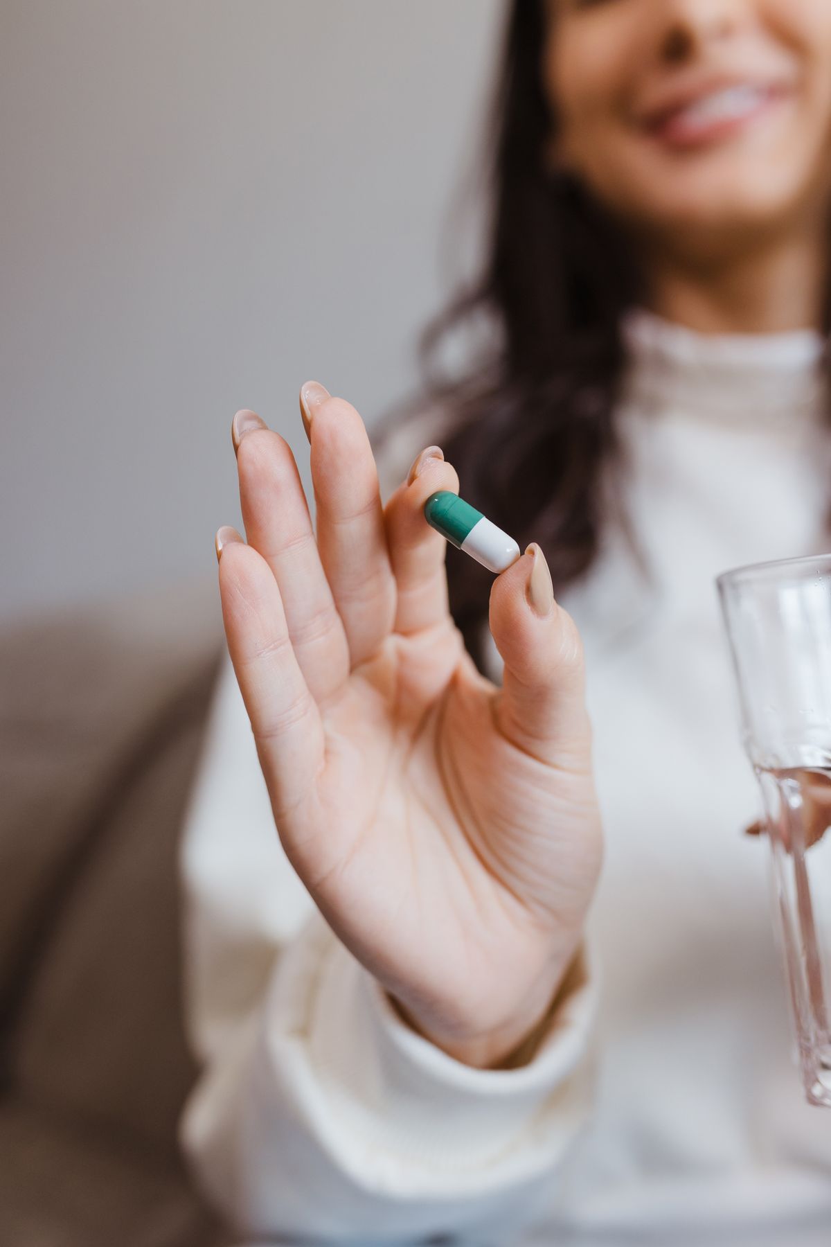 Femme souriante tenant une gélule et un verre d'eau, symbolisant une routine bien-être quotidienne